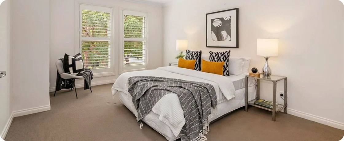 Bright, modern bedroom featuring a large bed, decorative pillows, and natural light from windows, enhancing the About page's ambiance.